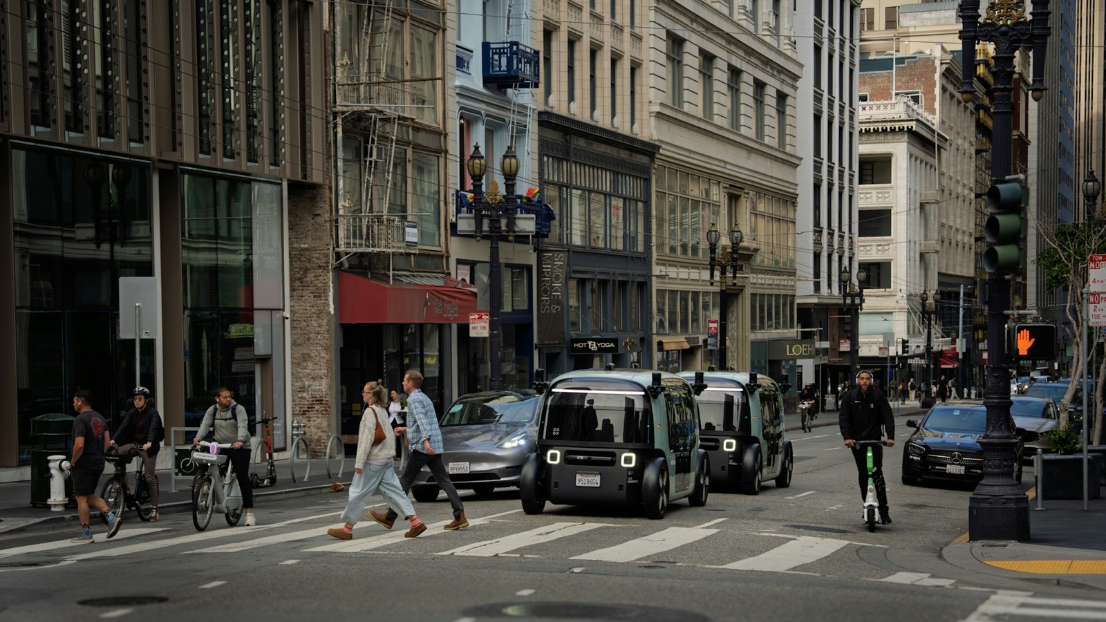 Two Zoox purpose-built electric robotaxis driving on a city street