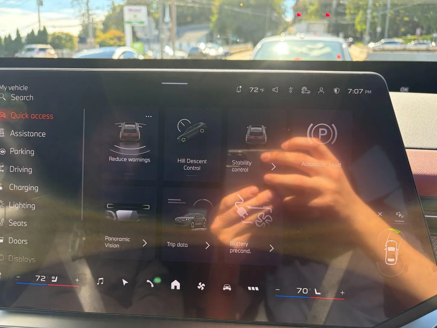 The BMW iX3 central touchscreen showing the Quick access menu with Assistance, Parking, Driving, Charging, Lighting and Seats in a column on the left, with sun glare on the glass