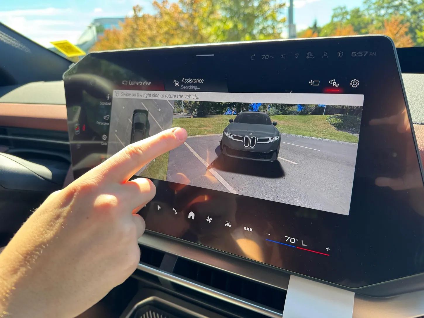 A hand swiping the BMW iX3 center touchscreen, which shows a 3D camera view of the gray SUV from the front