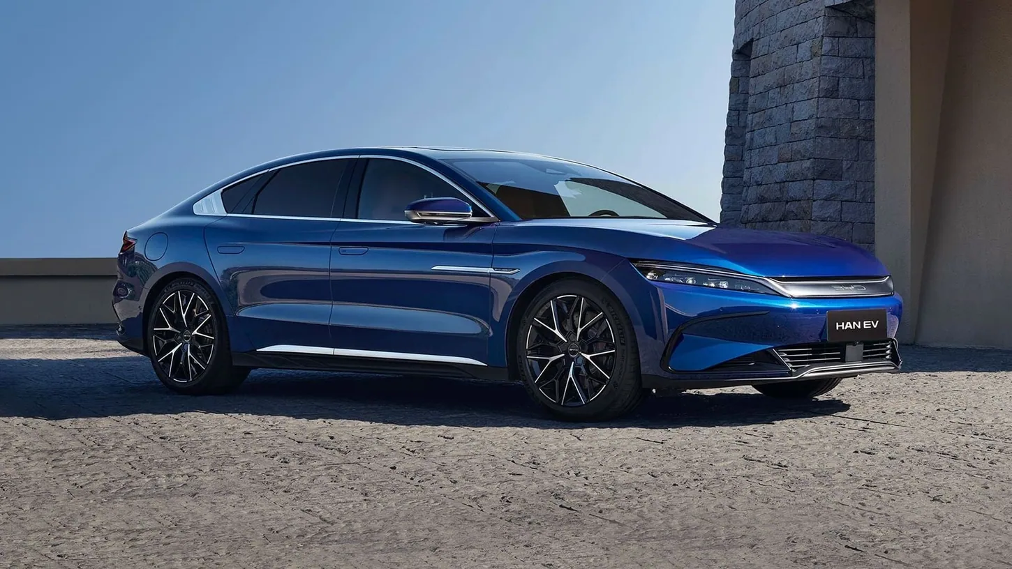 Blue BYD Han EV sedan parked in front of a stone wall under a clear sky