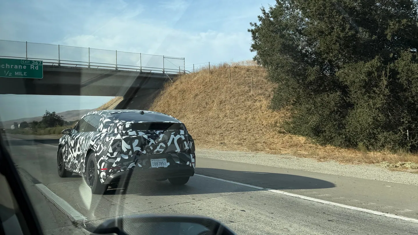 Camouflaged Lucid Cosmos prototype from behind on US-101 passing under the Cochrane Road overpass, photographed through a car window