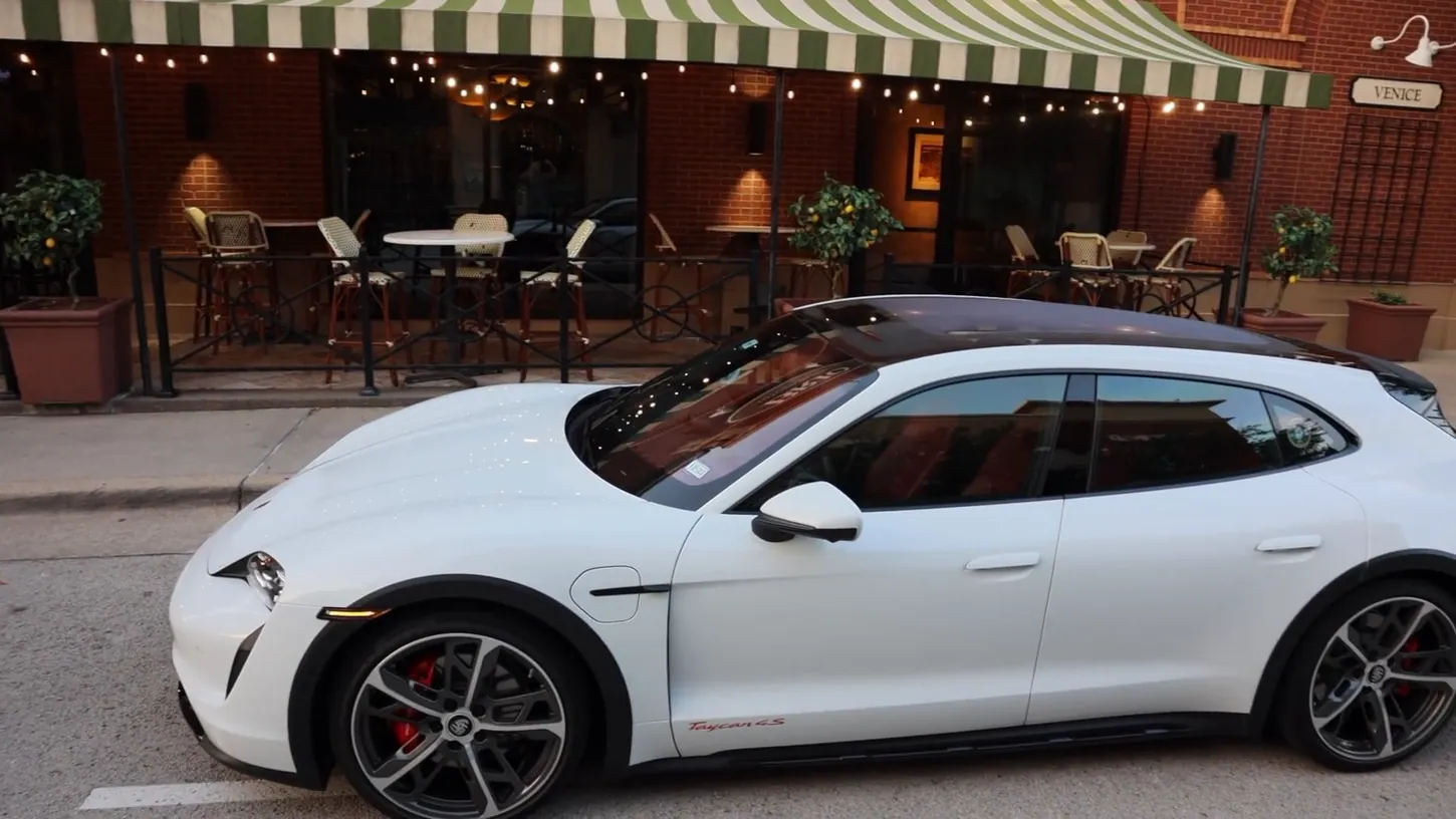 White 2023 Porsche Taycan 4S Cross Turismo parked in front of a restaurant patio with a striped awning
