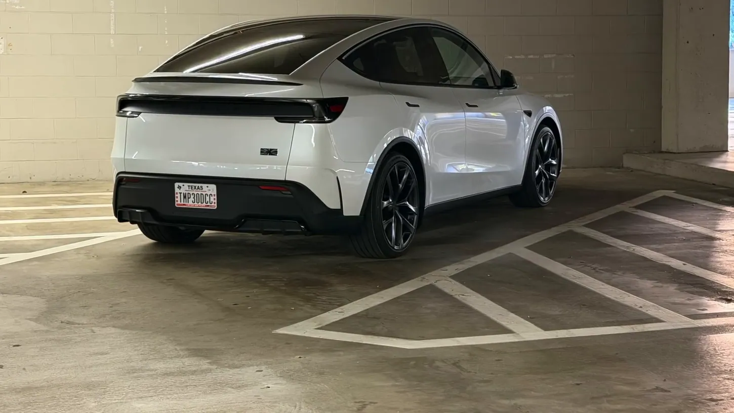 Rear three-quarter view of a white Tesla Model Y Performance with carbon fiber spoiler and black 21-inch wheels in a parking garage