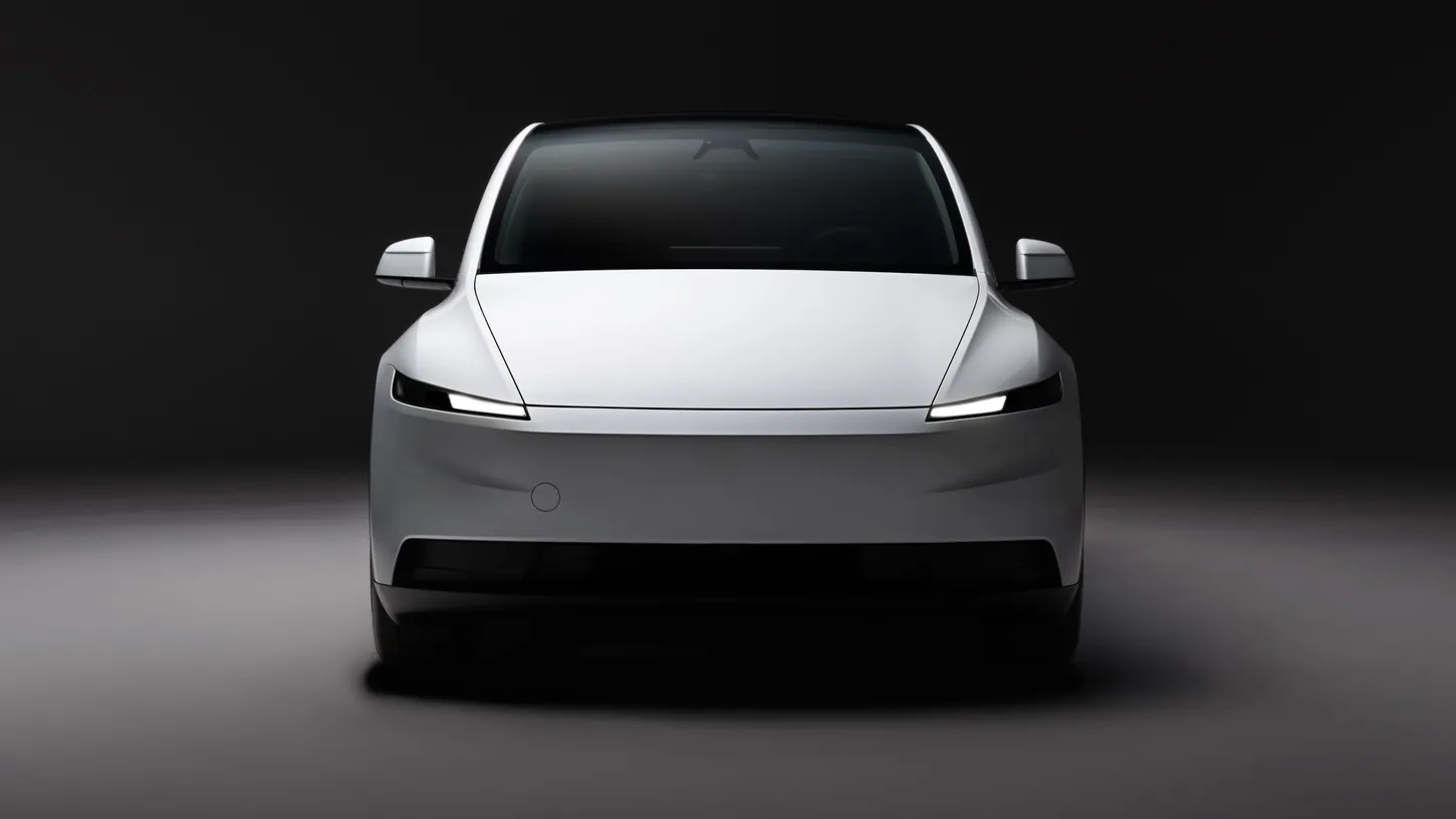 White Tesla Model Y photographed head-on in a dark studio with its headlights on
