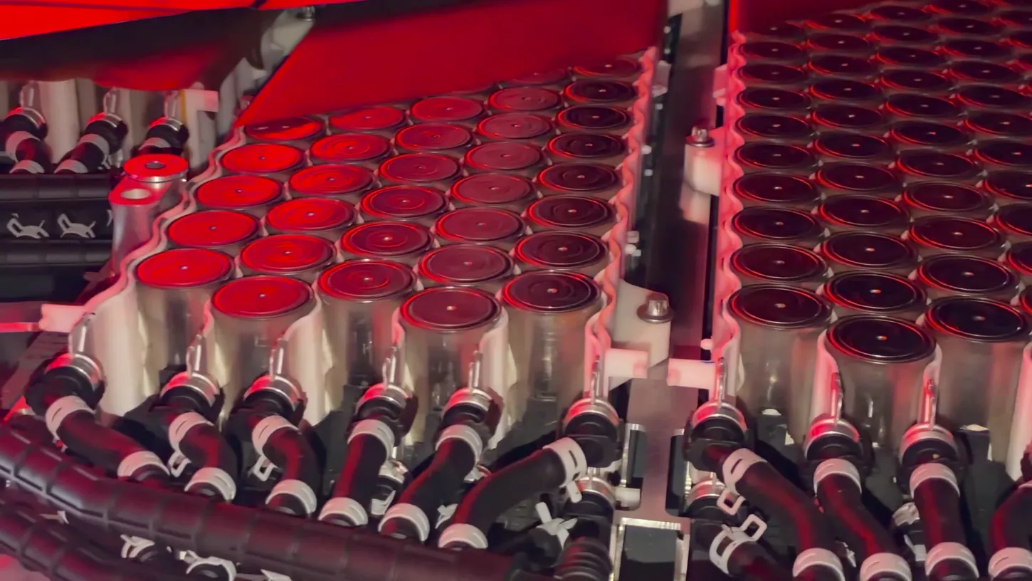 Cutaway of the Tesla Roadster battery display showing rows of cylindrical cells lit in red, with black hoses along the bottom