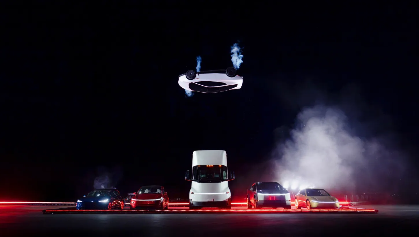 White Tesla Roadster upside down in midair with thruster plumes, above a row of a Model 3, Model Y, Semi, Cybertruck and Cybercab