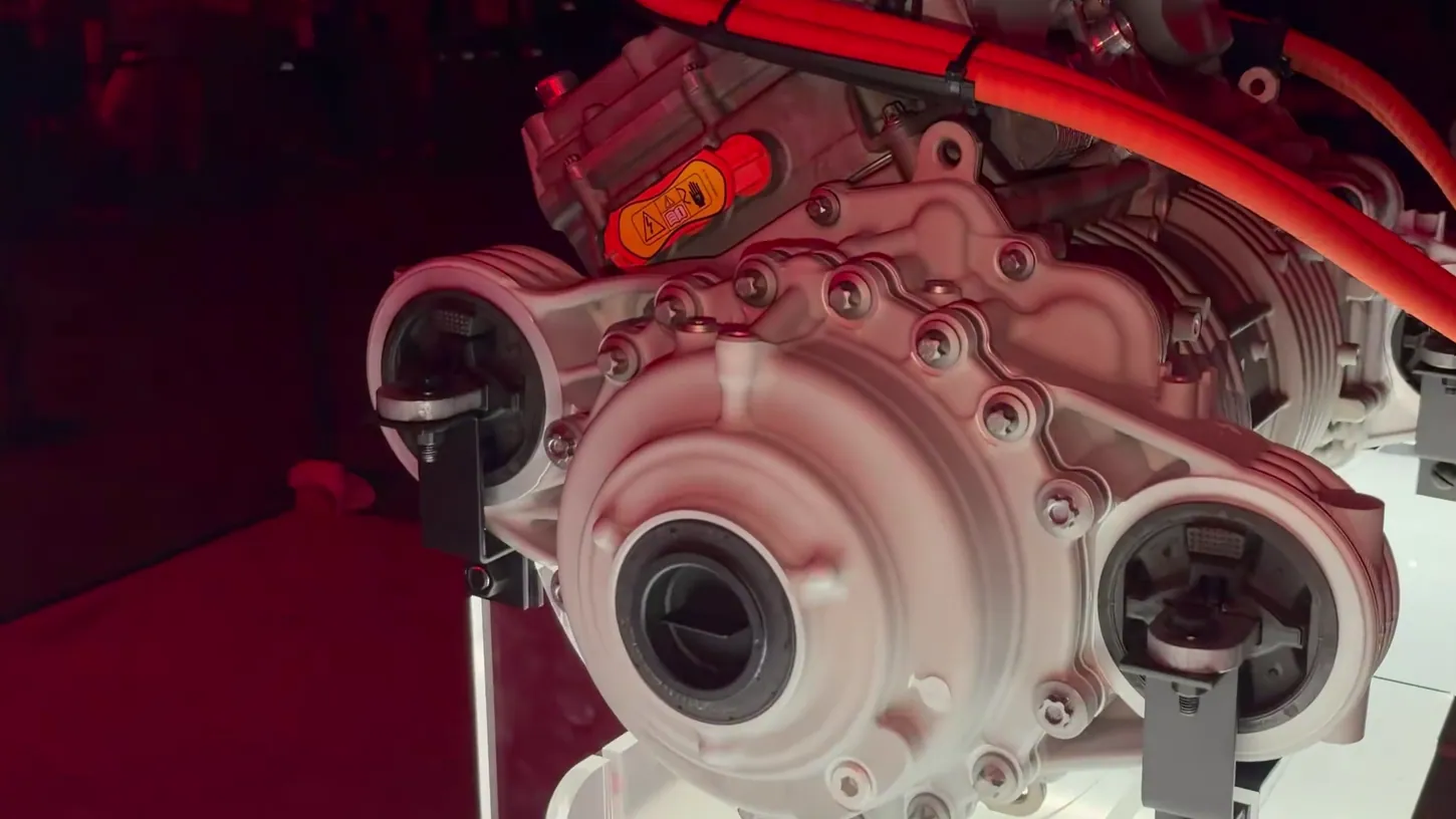 Close-up of the Tesla Roadster's rear drive unit on a lit display stand, with orange high-voltage cables running across the top
