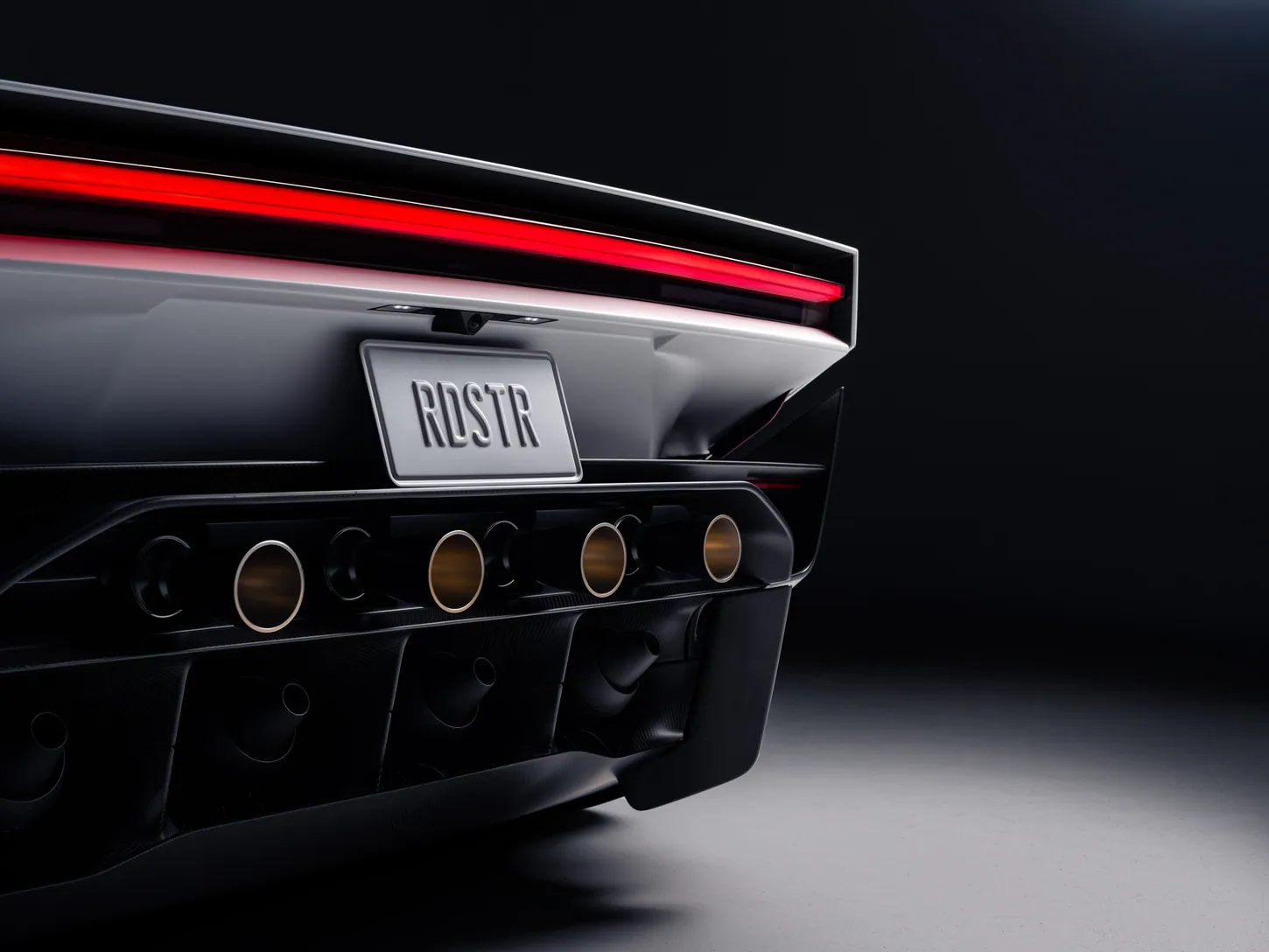 Close-up of a dark Tesla Roadster's rear with a red light bar, an RDSTR license plate and four gold-lined thruster nozzles below it