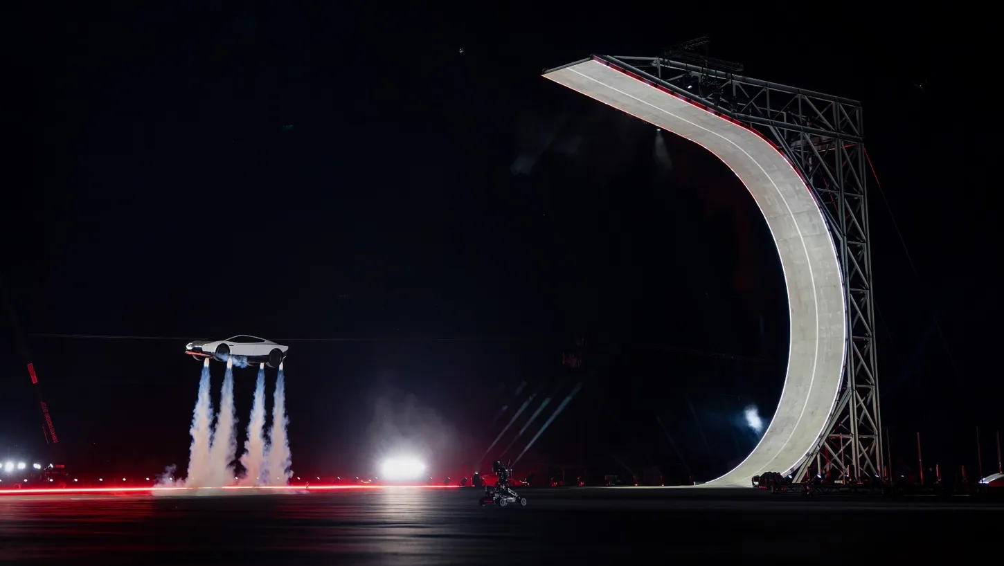 Tesla Roadster hovering on four white thruster plumes beside a tall curved ramp lit at night