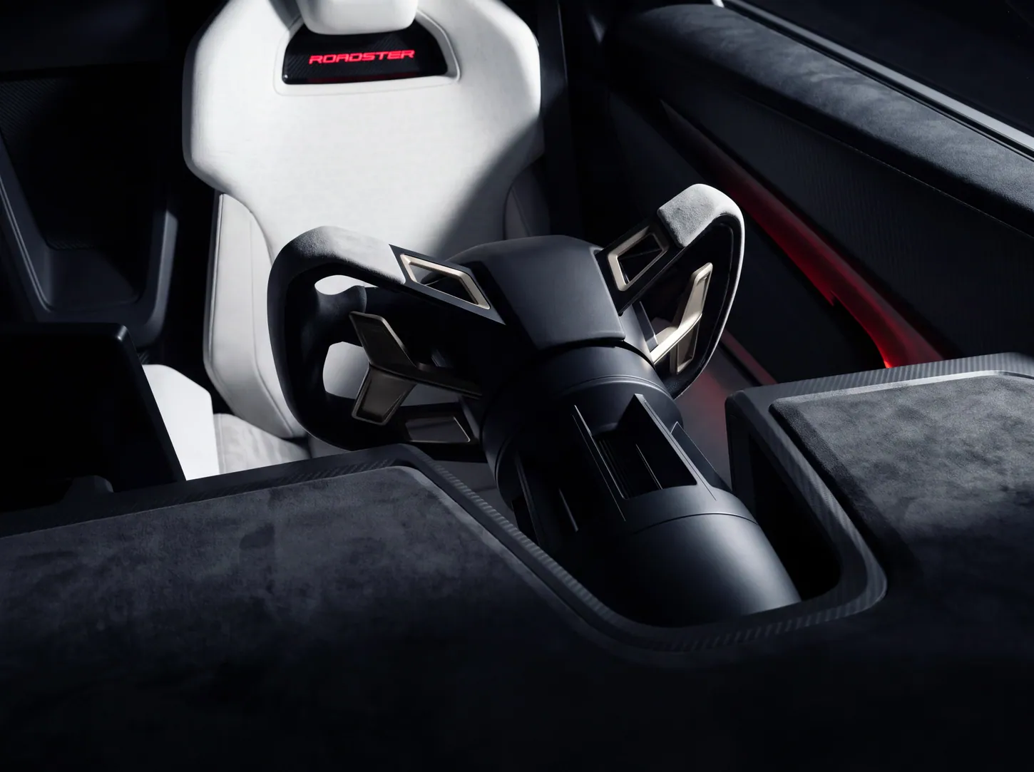 Close-up of the Tesla Roadster yoke on its black steering column, in front of a white seat with an illuminated ROADSTER badge