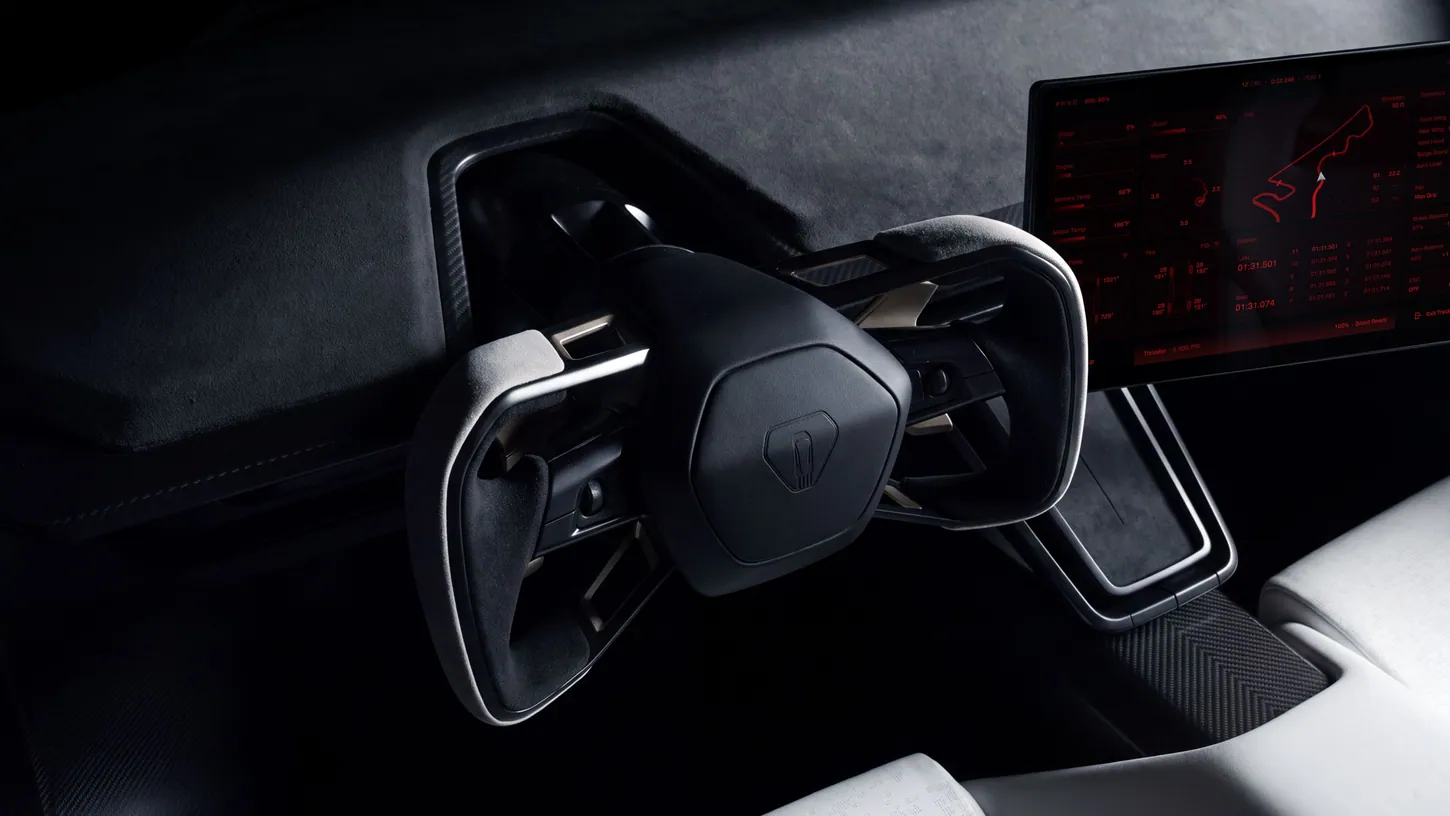 Close-up of the Tesla Roadster's gray microsuede yoke in front of a touchscreen showing a red Track Mode page with a circuit map and lap times
