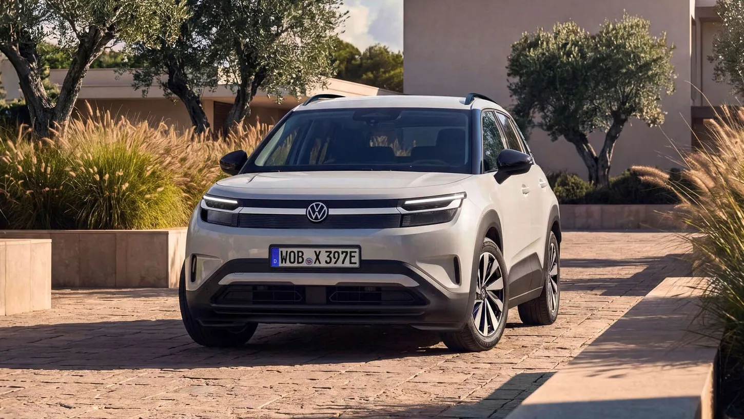White Volkswagen ID. Cross compact electric SUV parked head-on on a paved courtyard between olive trees and ornamental grasses