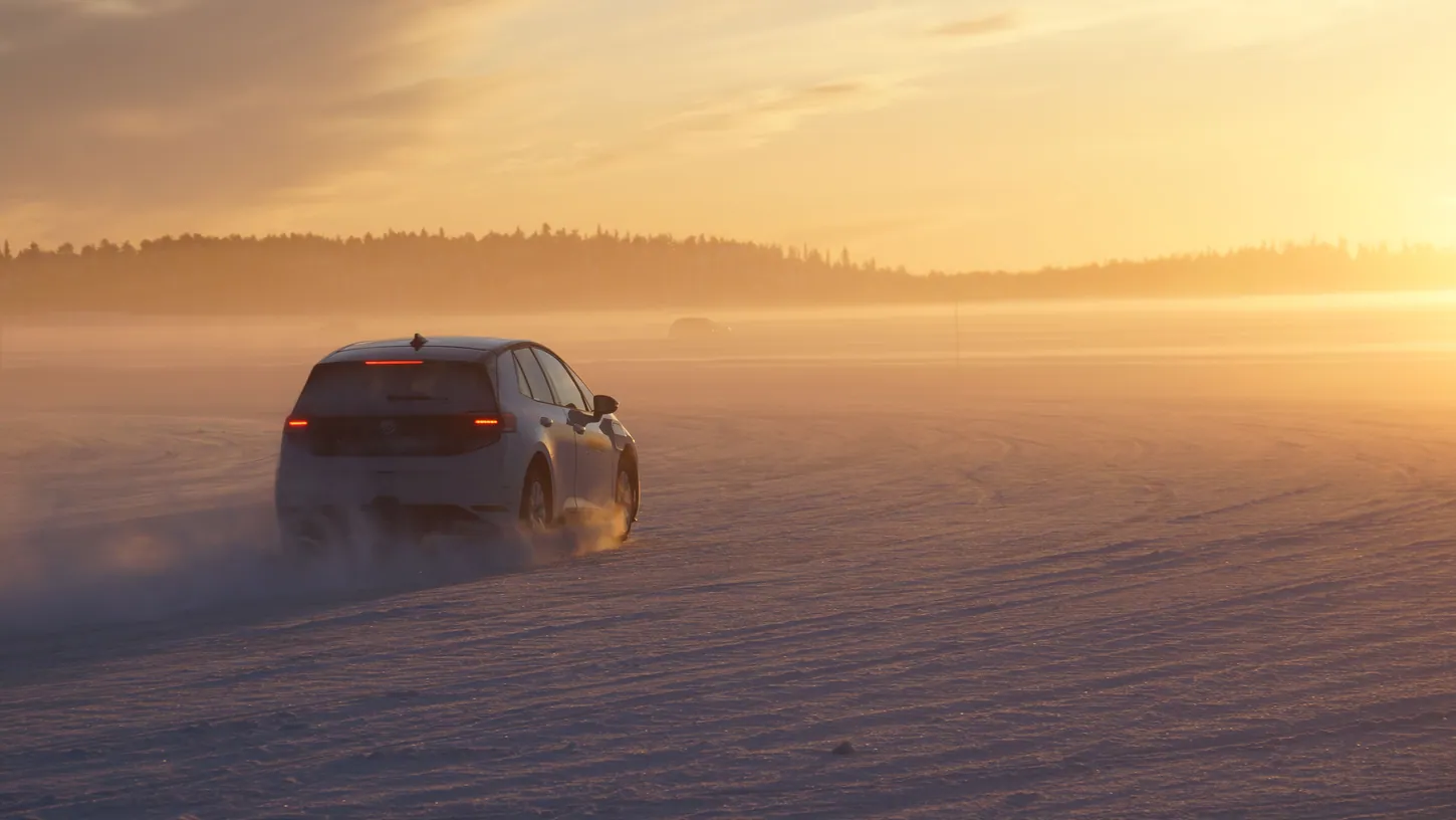 White Volkswagen ID.EVERY1 prototype driving away across a snow-covered frozen lake at sunset