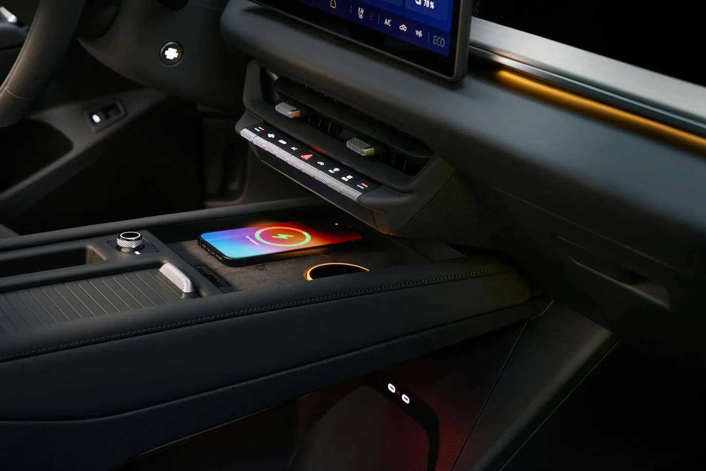 The ID. Tiguan center console with a row of physical climate buttons under the air vents and a phone on the Qi2 wireless charging pad