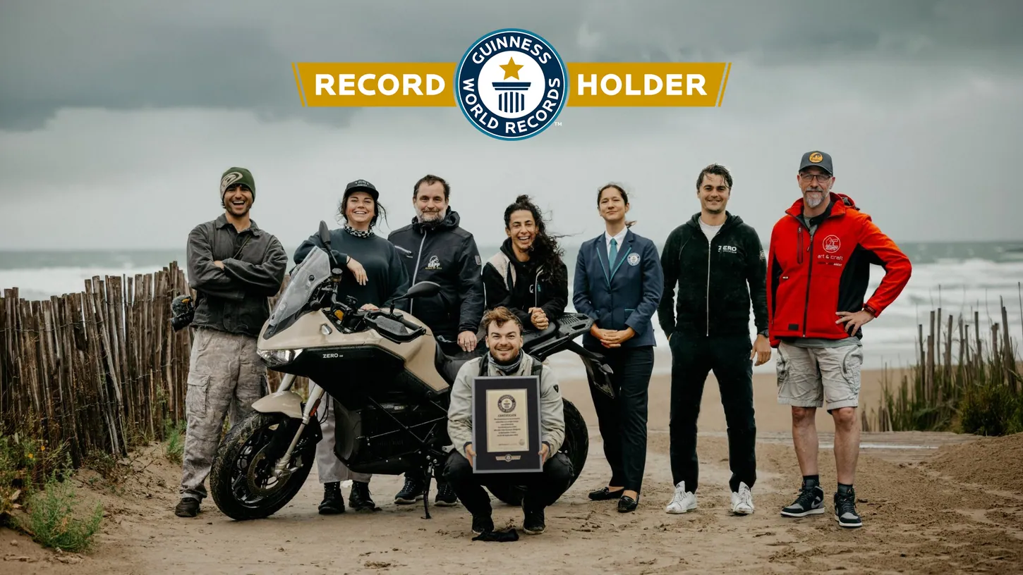 Eight people on a sandy beach path beside a beige Zero DS, one crouching with a framed Guinness World Records certificate, under a Guinness World Records Record Holder logo